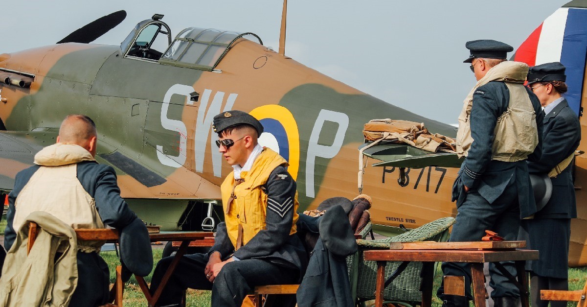 Personnel in uniform sit at tables by Spitfire model.
